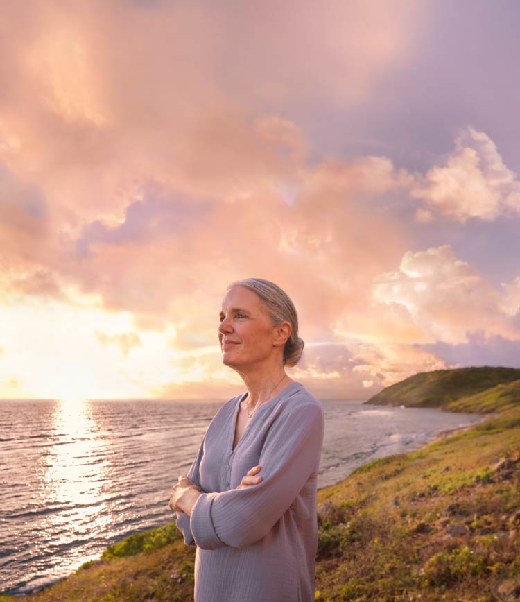 Smiling woman on hilltop watching sunrise over ocean